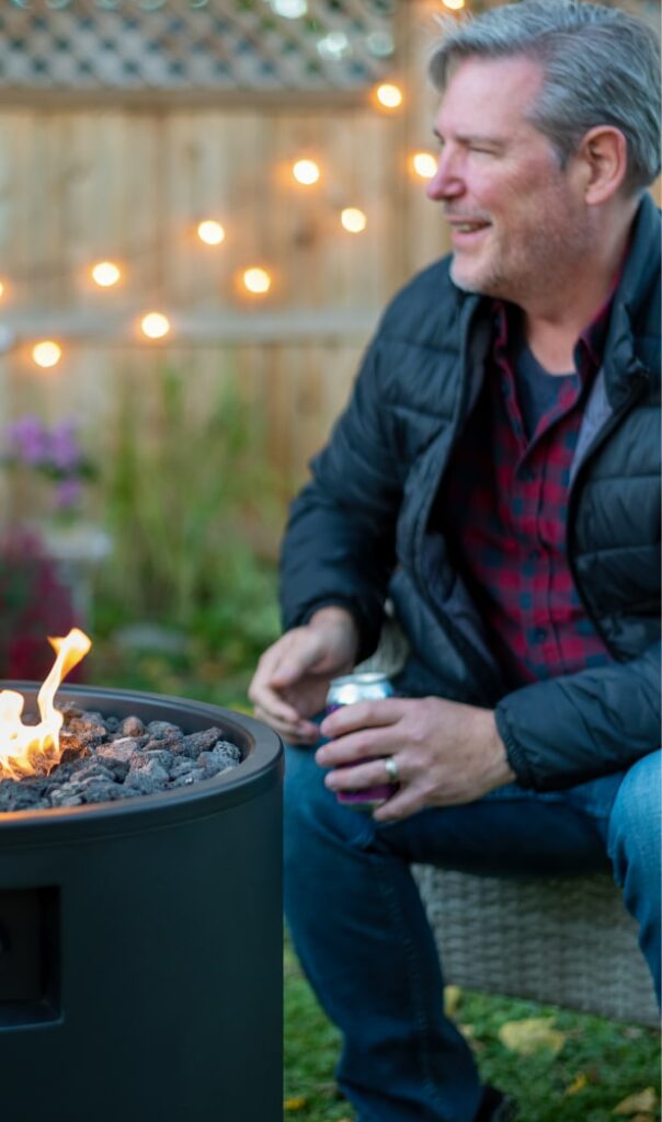 older man sitting by a fire pit with a beer